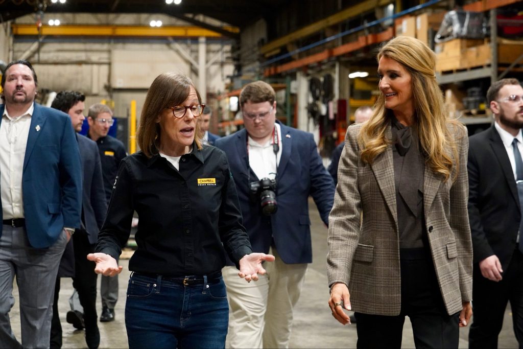 Administrator Loeffler walks with a woman business owner inside of their manufacturing warehouse along with press and SBA staffers