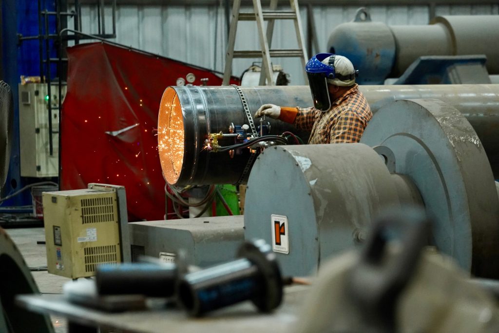 An American small manufacturer works on soldering a pipe while inside of an industrial warehouse